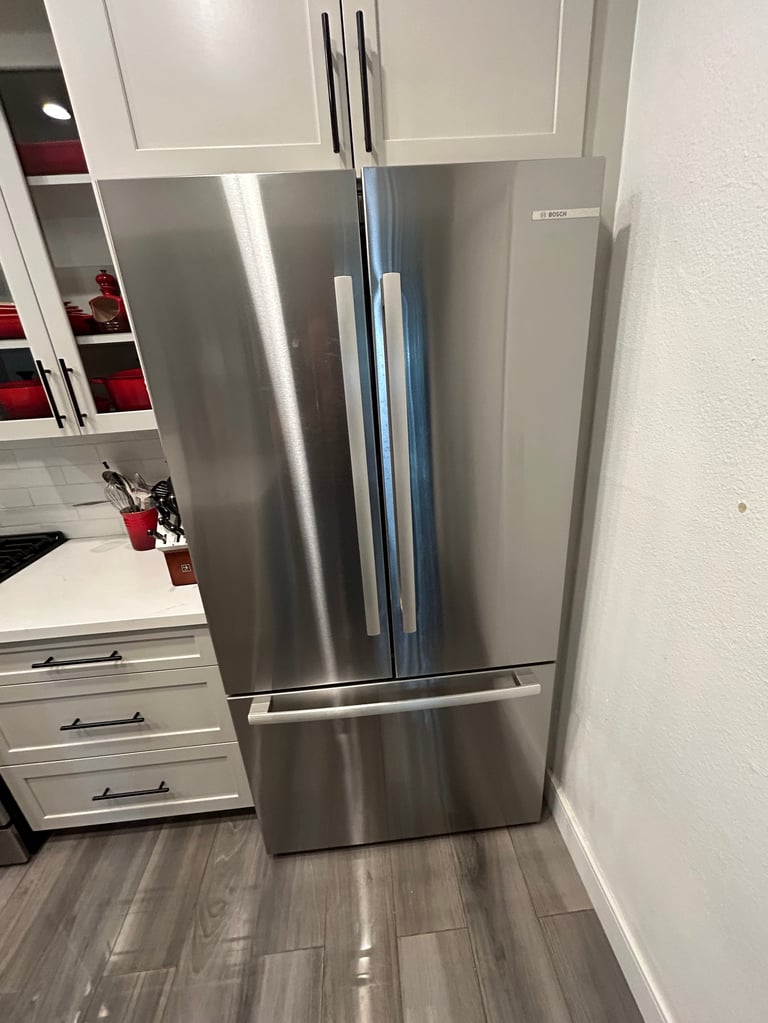 Stainless steel French door refrigerator in modern kitchen with white cabinets and wood-look flooring
