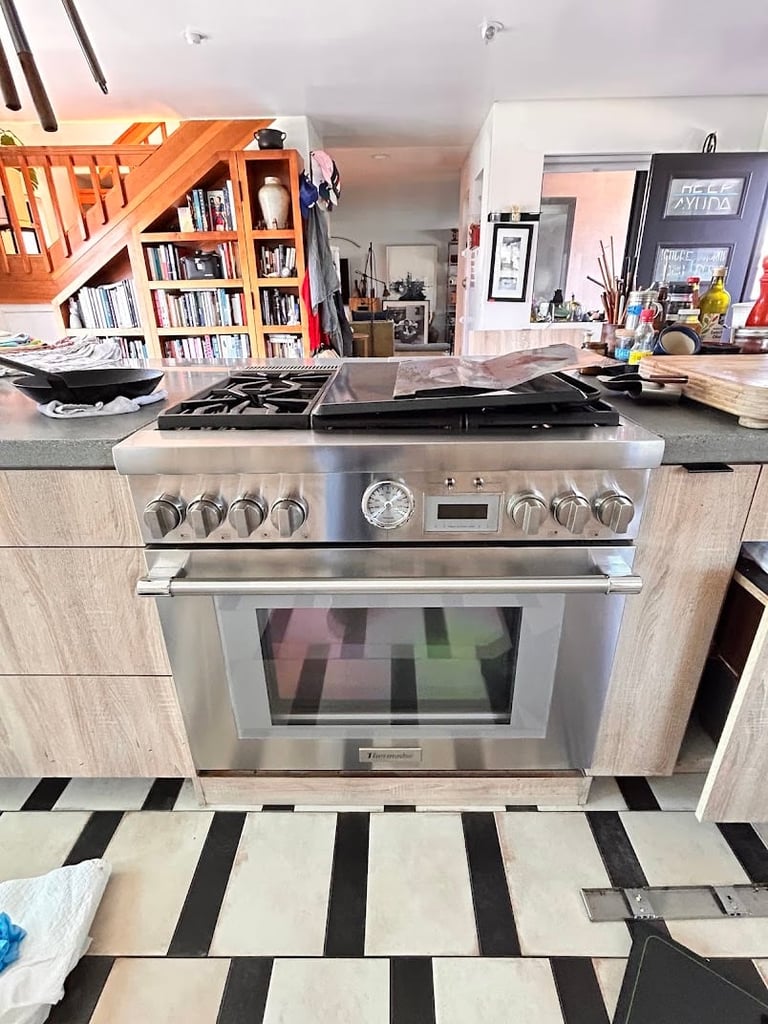 Stainless steel kitchen range with gas cooktop and oven in open-concept home with bookshelf and striped floor