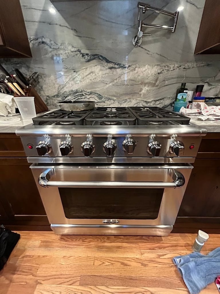 Stainless steel professional gas range with six burners and oven in a modern kitchen with marble backsplash