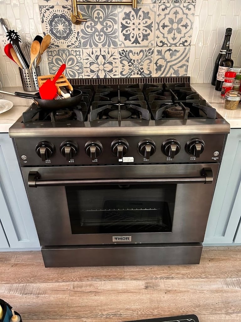 Stainless steel Thor gas range with six burners in a kitchen with patterned tile backsplash and cooking utensils on counter