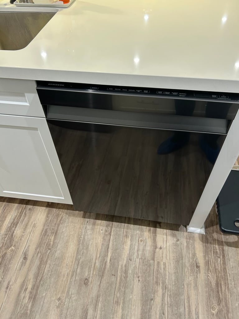 Black dishwasher installed in white kitchen cabinet with wood-look flooring below